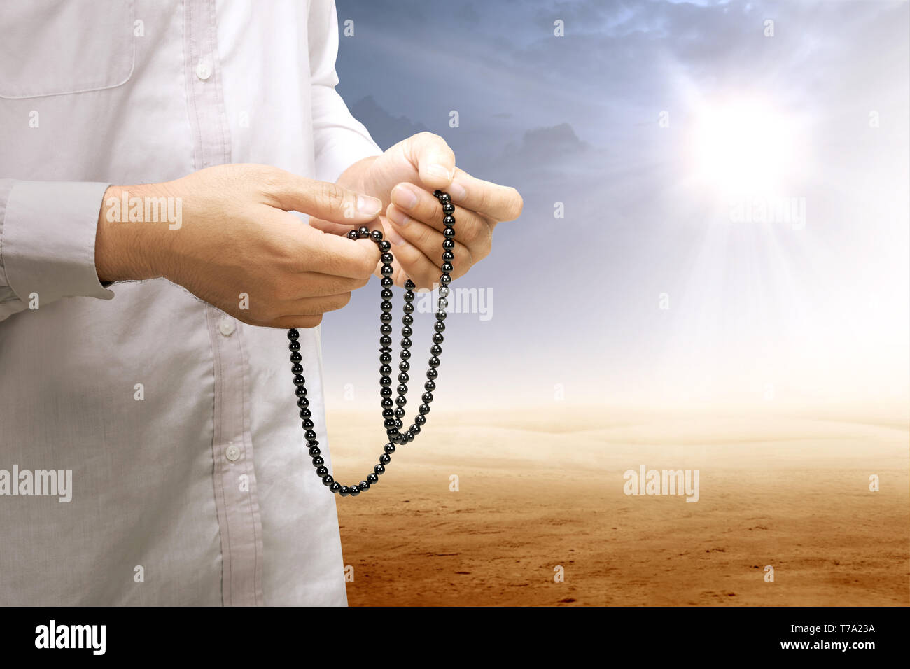 Muslim man praying with prayer beads on his hands on desert with sun ...