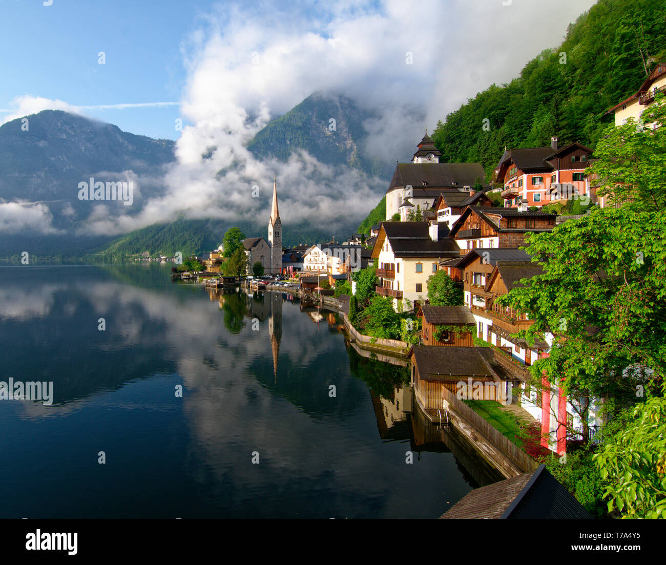 Early morning shot of Hallstatt village and reflections in the still water of Hallstatter See (Lake Hallstatt) with low cloud on the hillside Stock Photo