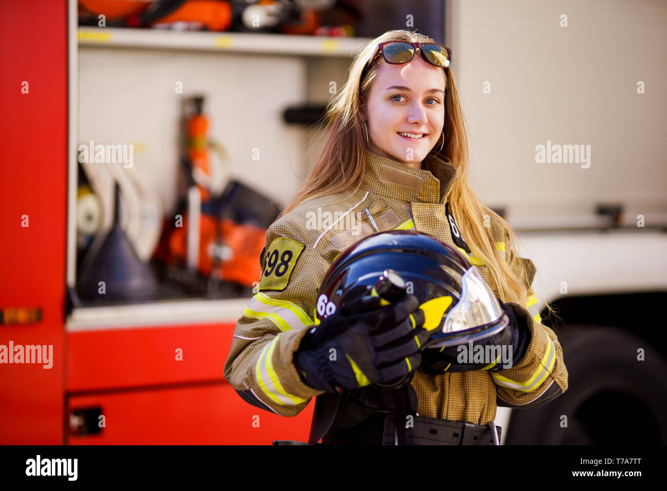 Image of woman firefighter with helmet in her hands standing near fire