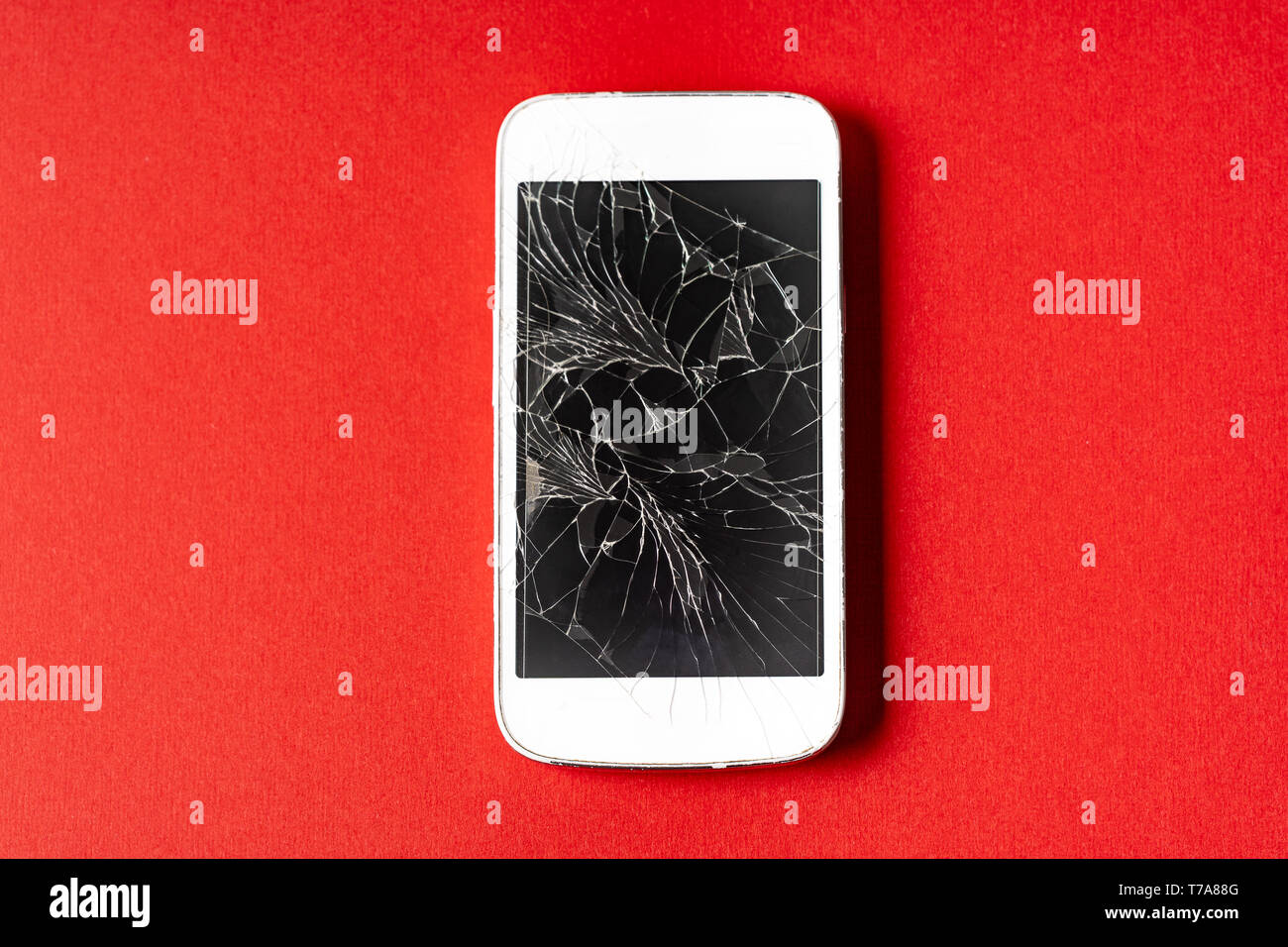 Broken mobile phone with cracked display on red background, flat lay. Stock Photo