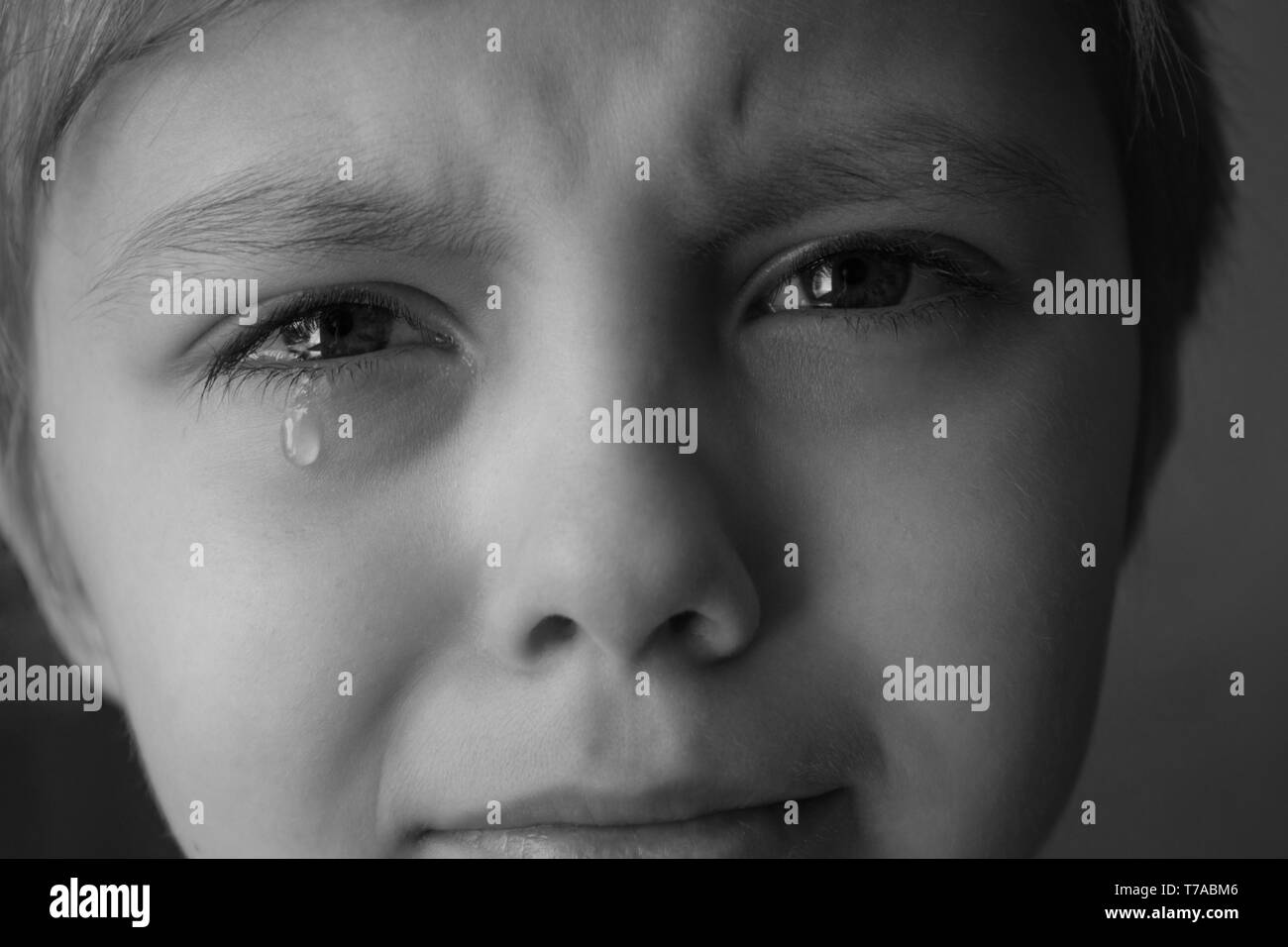 Tears in the eyes of a child. A tear on the boy's cheek. Close-up. Black and white photo. Stock Photo