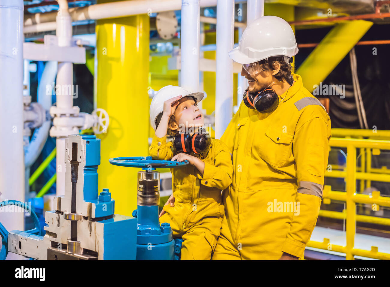 Young man and a little boy are both in a yellow work uniform, glasses, and helmet in an industrial environment, oil Platform or liquefied gas plant Stock Photo