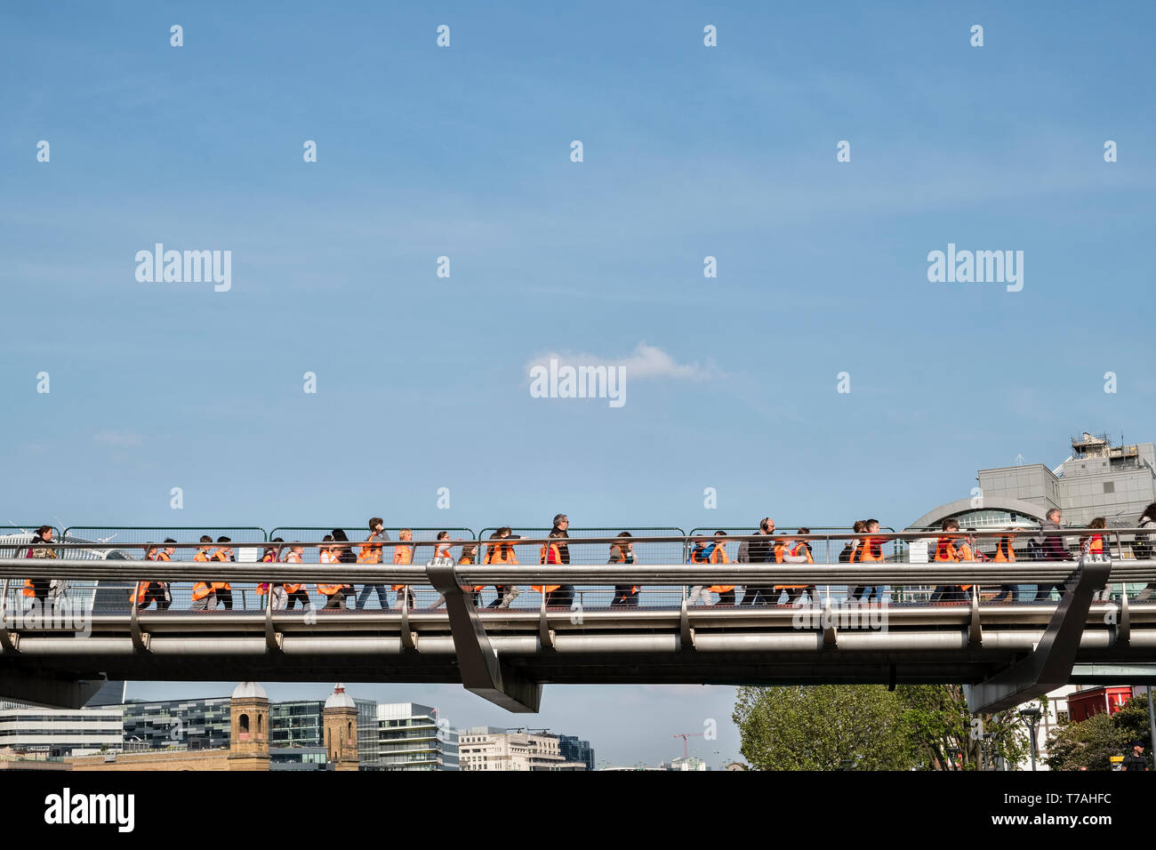 School children wearing hi-vis jackets crossing the Millennium Bridge over the River Thames in London, on their way to visit the Tate Modern gallery Stock Photo