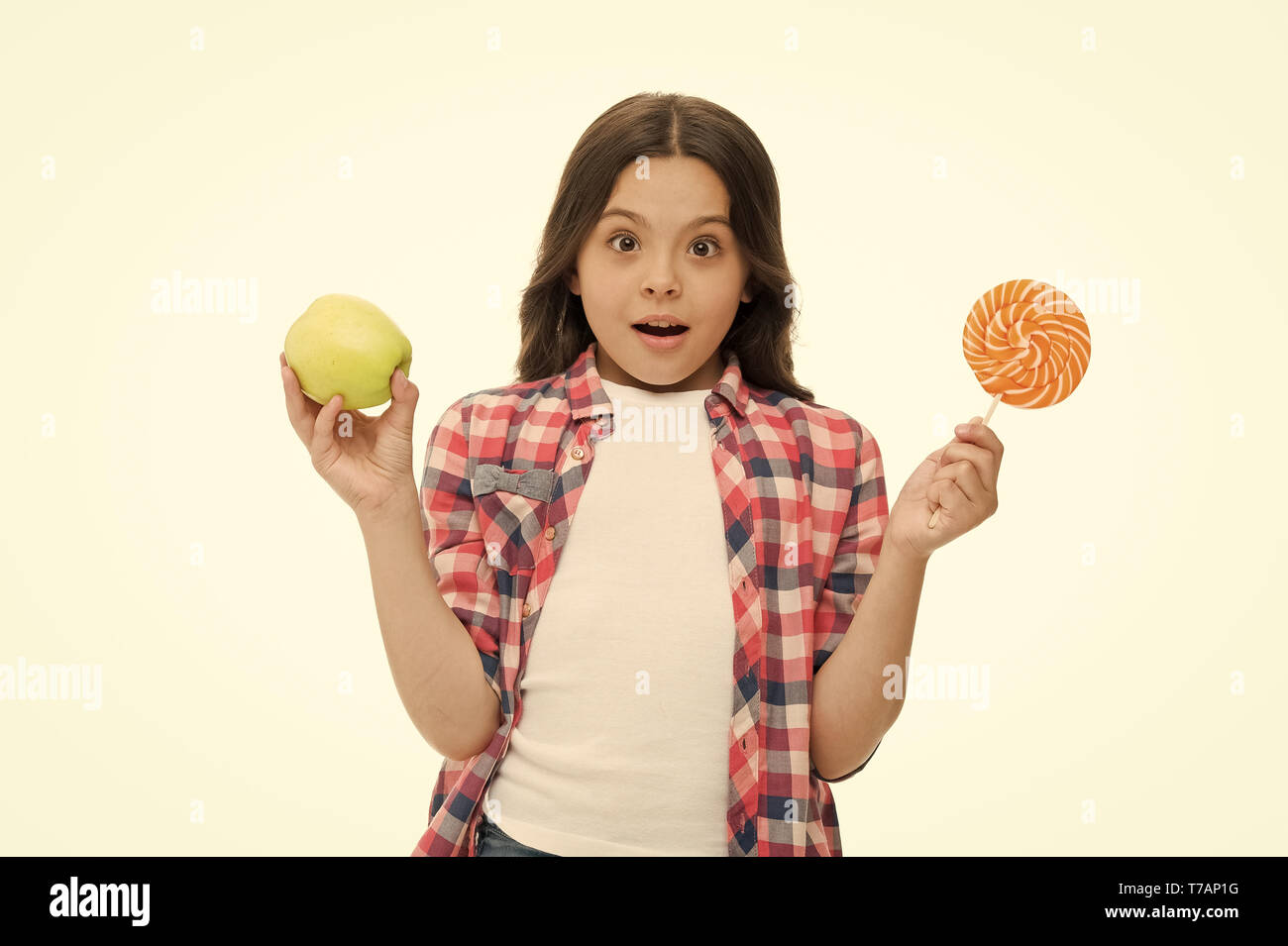 Can sugar sweet taste make us happy. Girl cute smiling face holds sweet lollipop and apple. School lunch alternatives. Girl likes sweet candy isolated white. Same sweet taste of apple and candy. Stock Photo