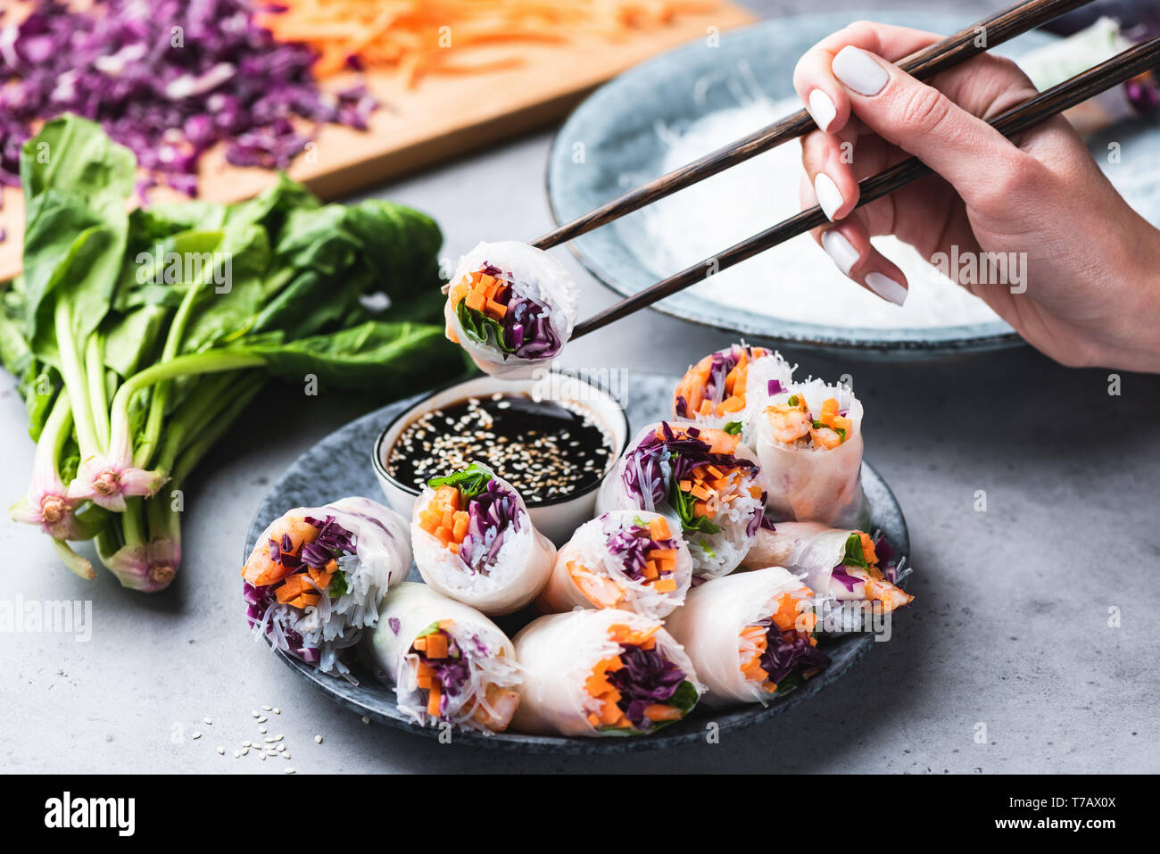 Eating Asian Cuisine Spring Rolls Or Rice Paper Rolls With Vegetables And Shrimps. Hand Holding Roll With Chopsticks Stock Photo