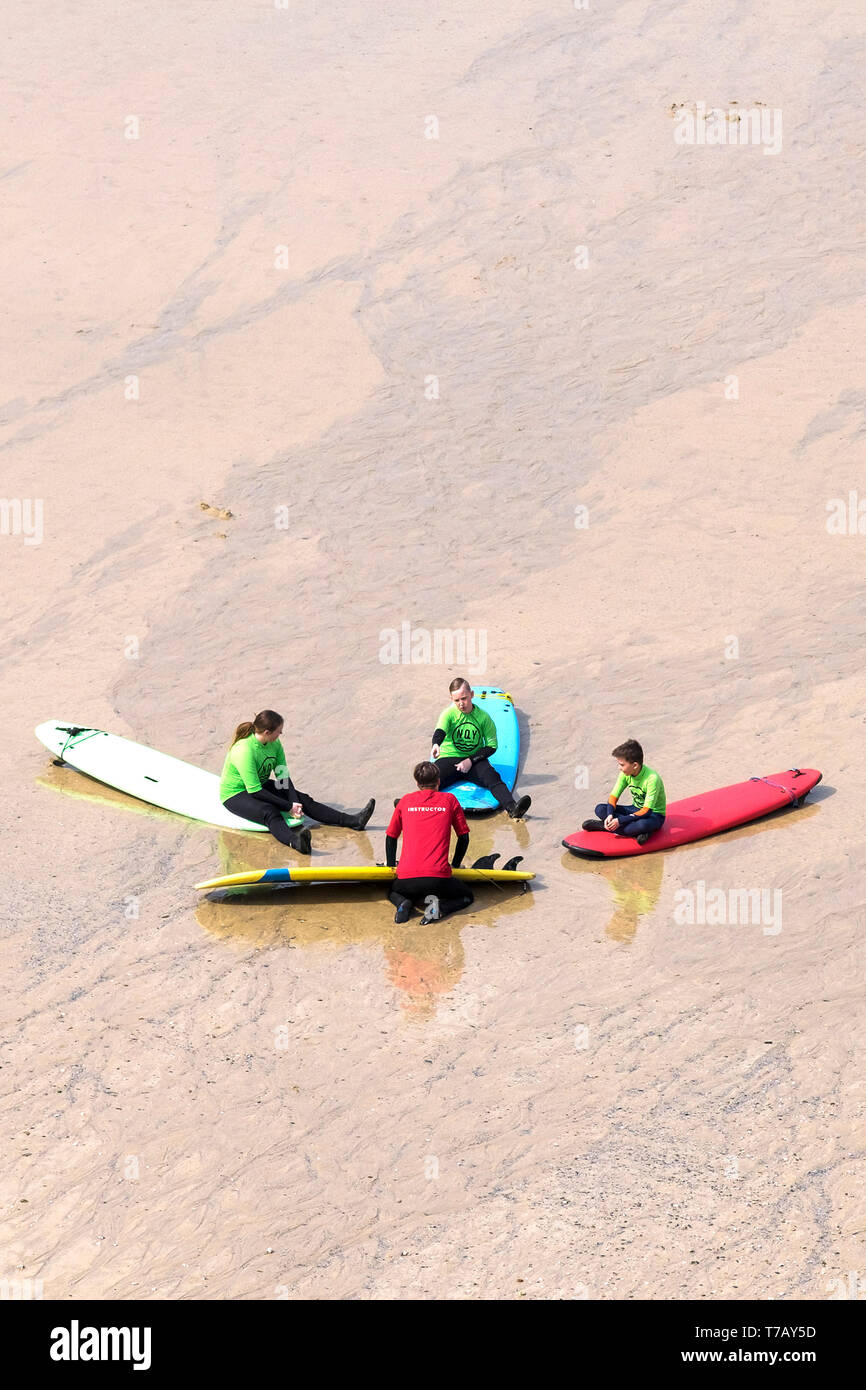 Young holidaymakers listening to their surf instructor during a surfing lesson on Great Western