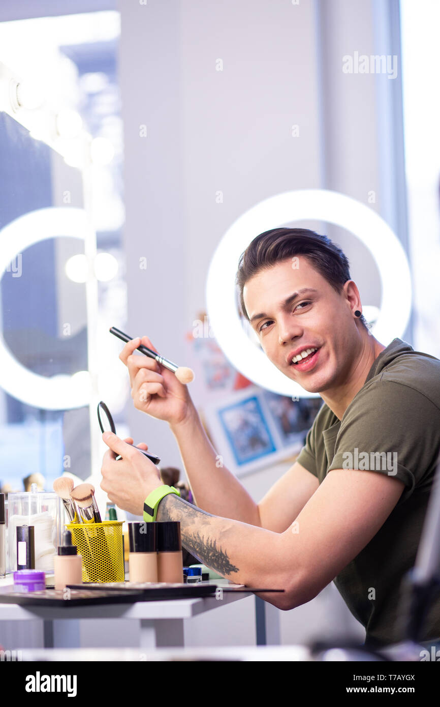 Dark-haired handsome man carrying makeup brush and skin powder Stock Photo