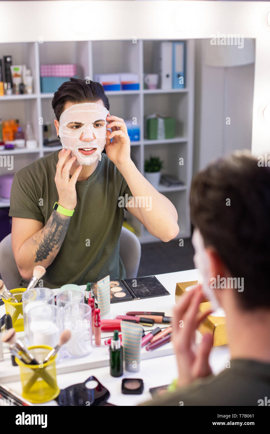 Satisfied young guy treating his skin with moisturizing mask Stock Photo