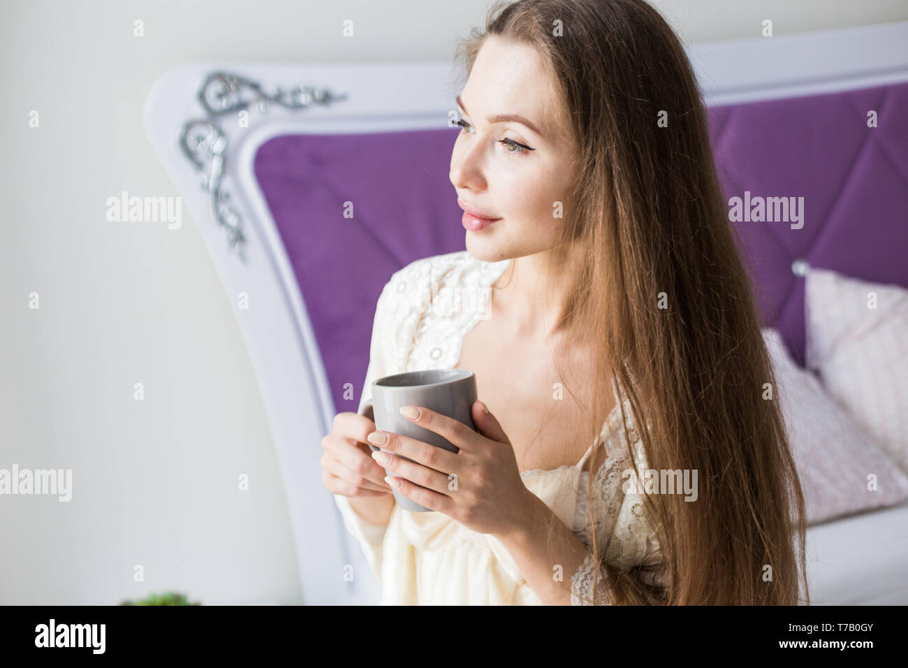 Attractive young girl in nightwear sits on the edge of the bed by the ...
