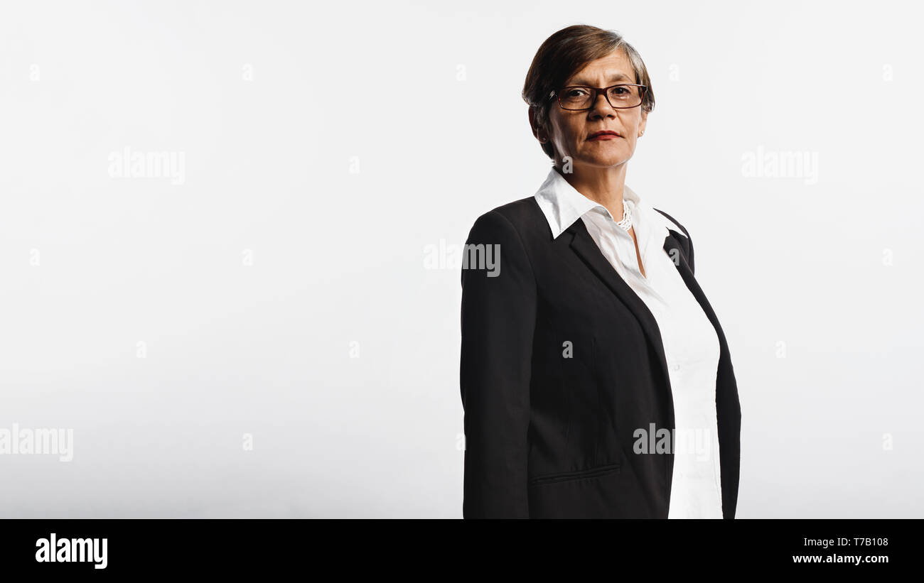 Side view of a senior woman in eyeglasses wearing a formal business attire. Woman looking at camera standing on white background. Stock Photo