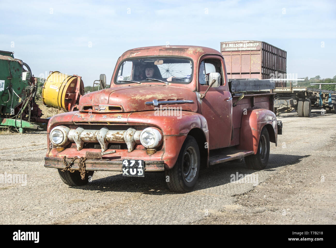 Rough rusty old vintage, classic Ford pickup truck driving through a farm with discarded ...