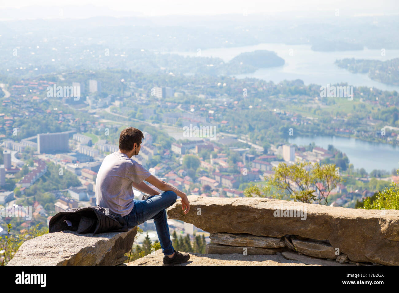 Man sitting alone, listening to music, looking at scenic views over Bergen, Norway from Ulriken Mountain Stock Photo