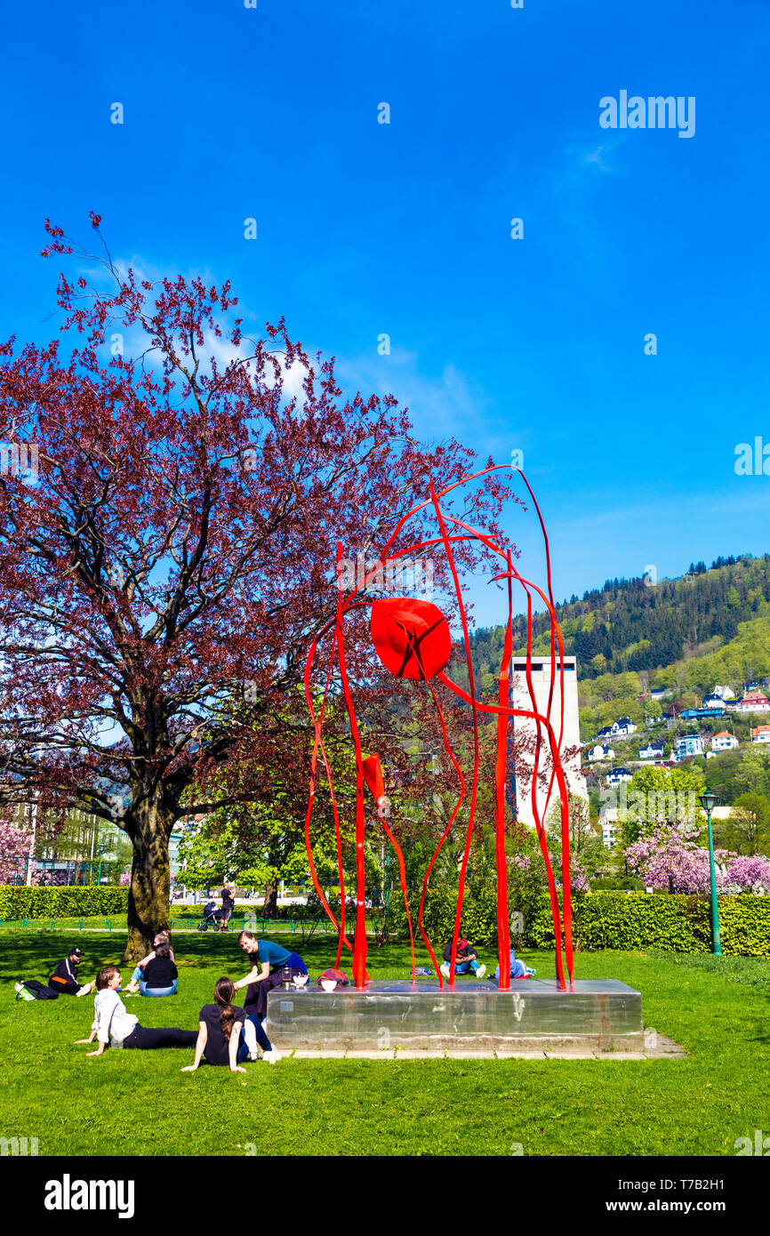 People sitting on grass, having picnic on a sunny day by 'Red Wind' abstract sculpture by Arnold Haukeland (1978) in Bergen, Norway Stock Photo