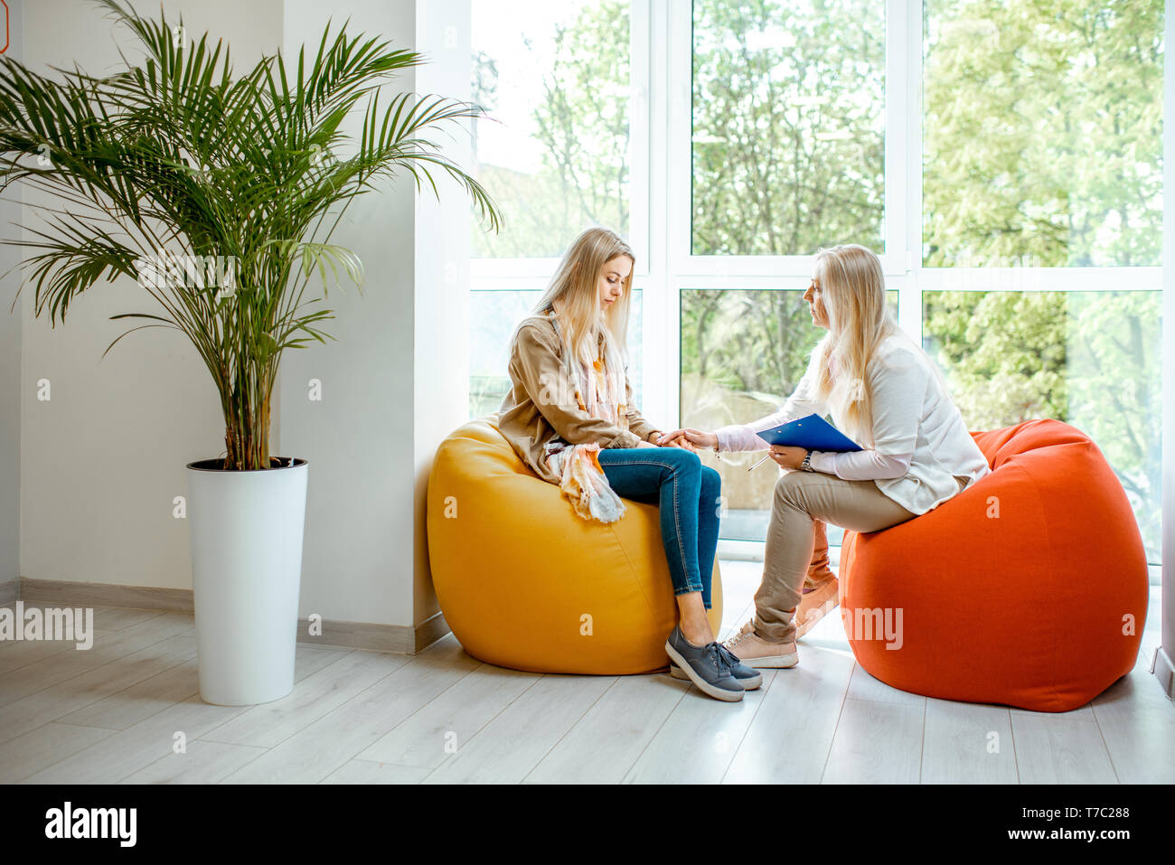 Young woman with senior female psychologist or mental coach sitting on the comfortable chairs during the psychological counseling in the office Stock Photo