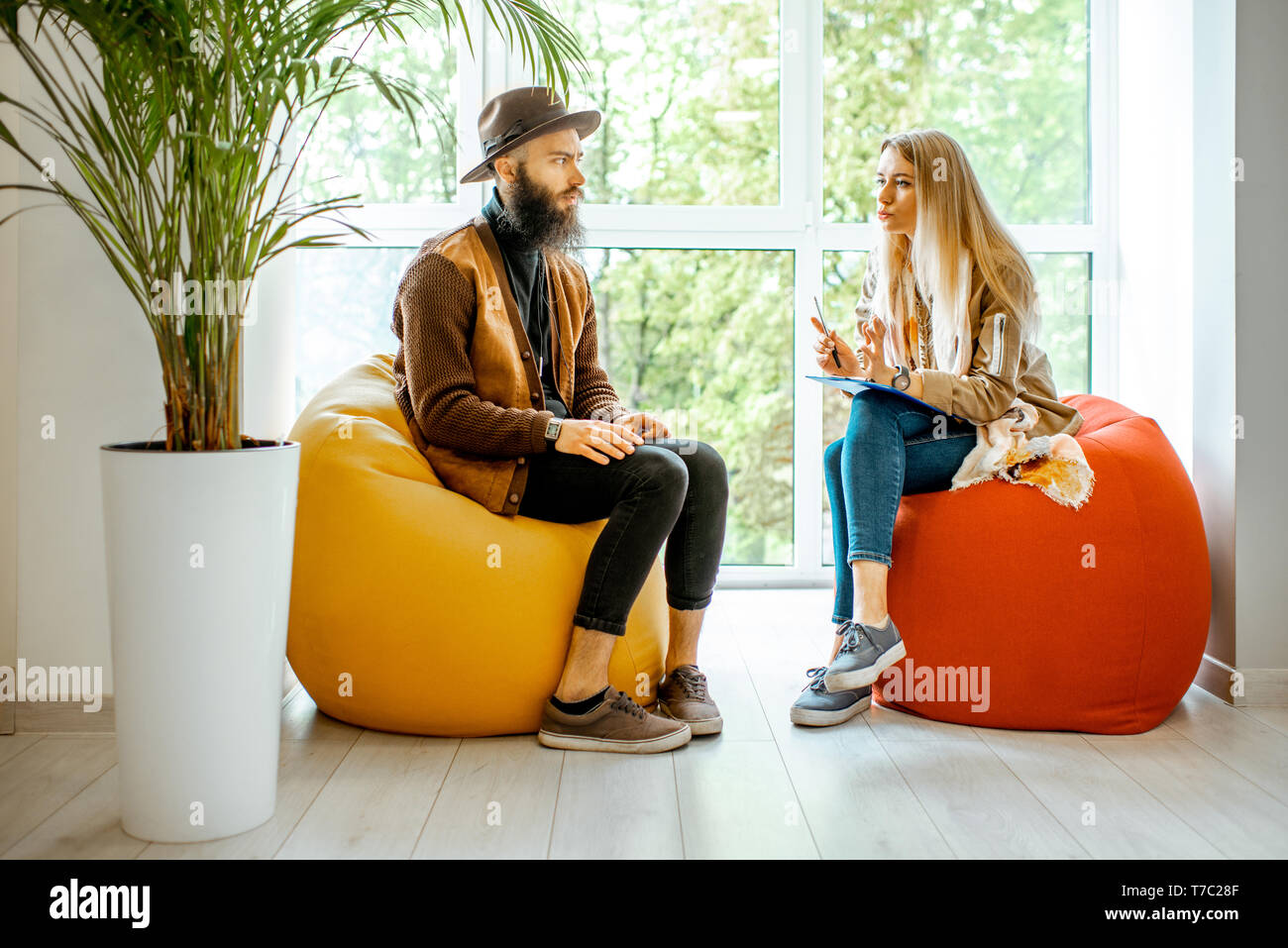 Young man and woman sitting on the comfortable chairs during the psychological counseling, solving some psychological problems in the office Stock Photo