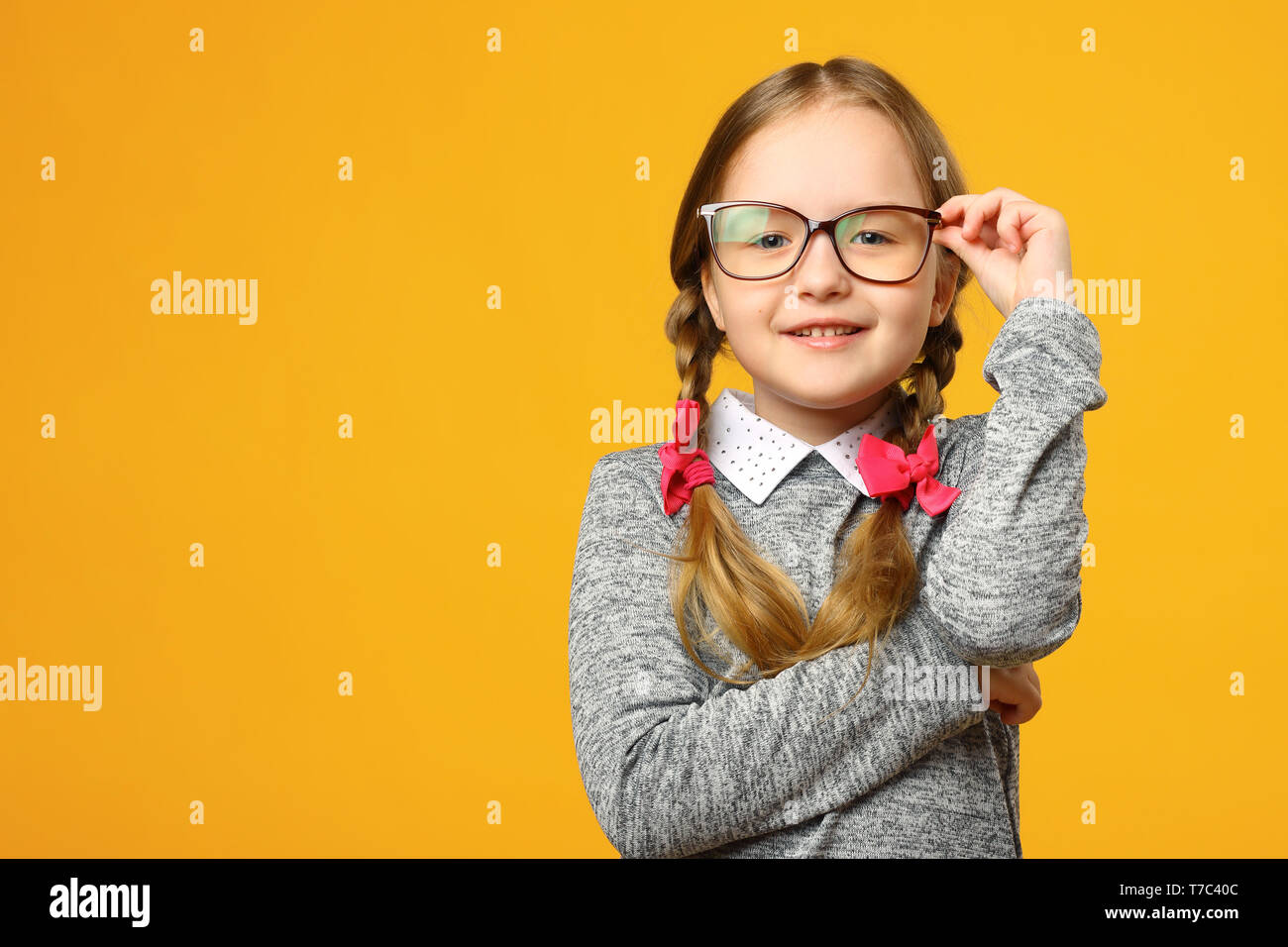 Portrait of a cute little kid girl in glasses on a yellow background. Child schoolgirl looking at the camera. The concept of education. Copy space. Stock Photo
