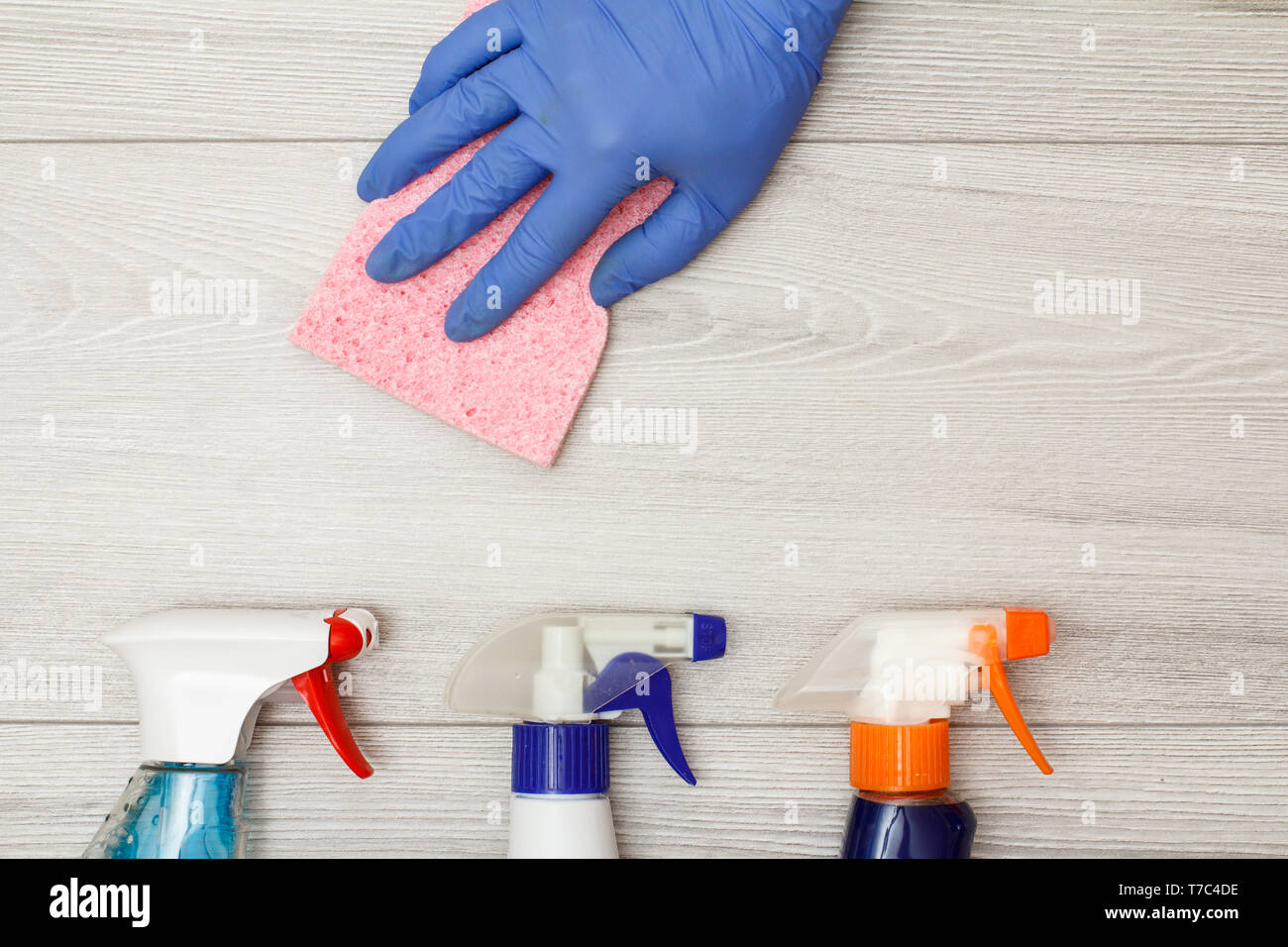 Hand in rubber glove holding pink napkin with bottles of detergent on ...