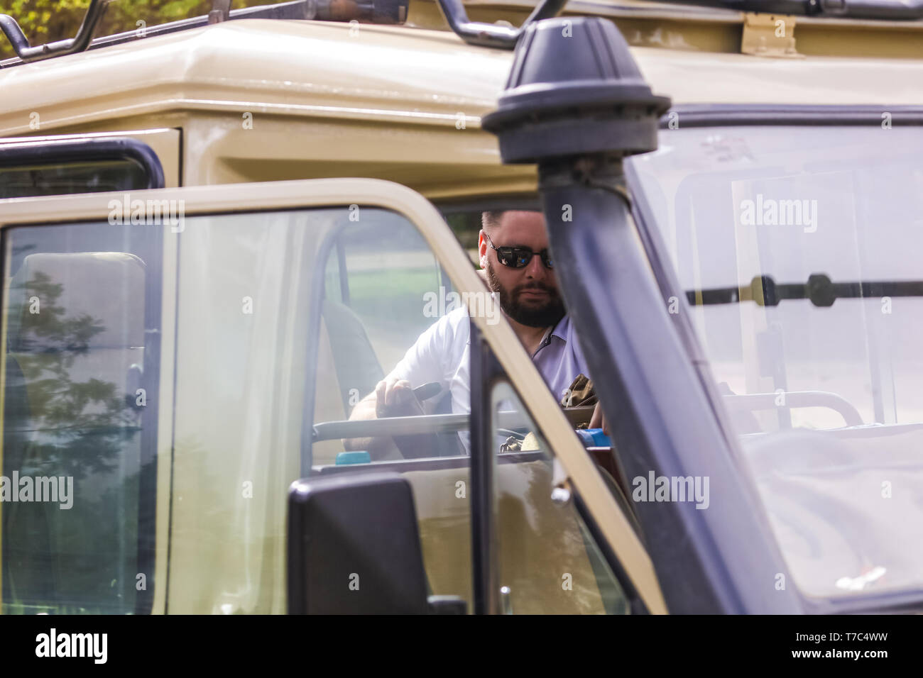 Serious man sitting in the car, sunglasses on his face, beard. Travel all over the Africa, go on safari, climbing on mountain, extreme vacation. Drive Stock Photo