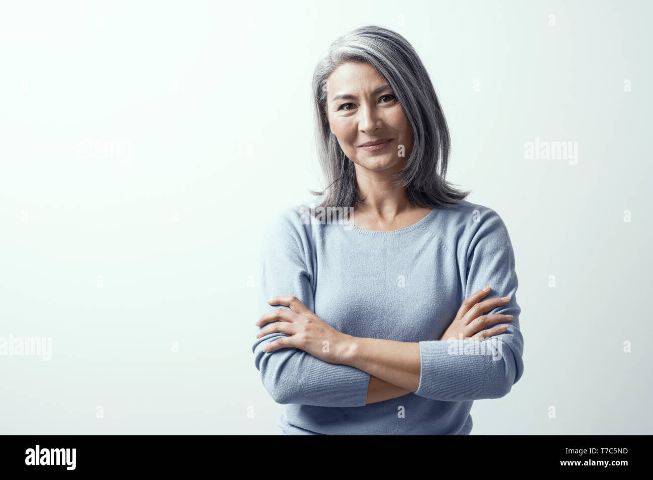 Beautiful Asian Woman with Grey Hair and Dark Skin Stands on a White