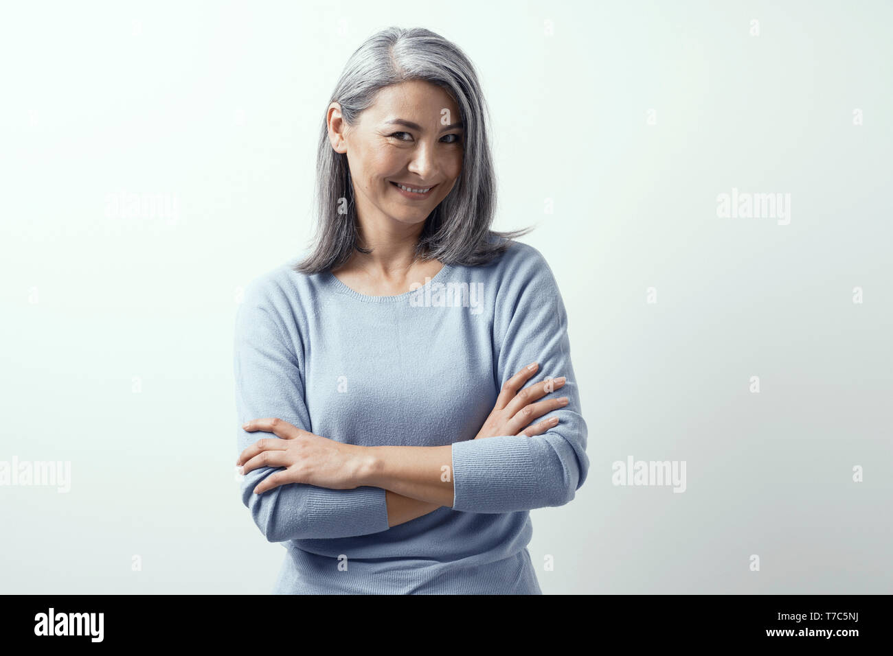 Charming Asian Middle-Aged Model with Dark Skin Posing on a White Background in Studio Smiling. Her Head Tilted Coquettishly. She Wears Blue Sweater. Stock Photo