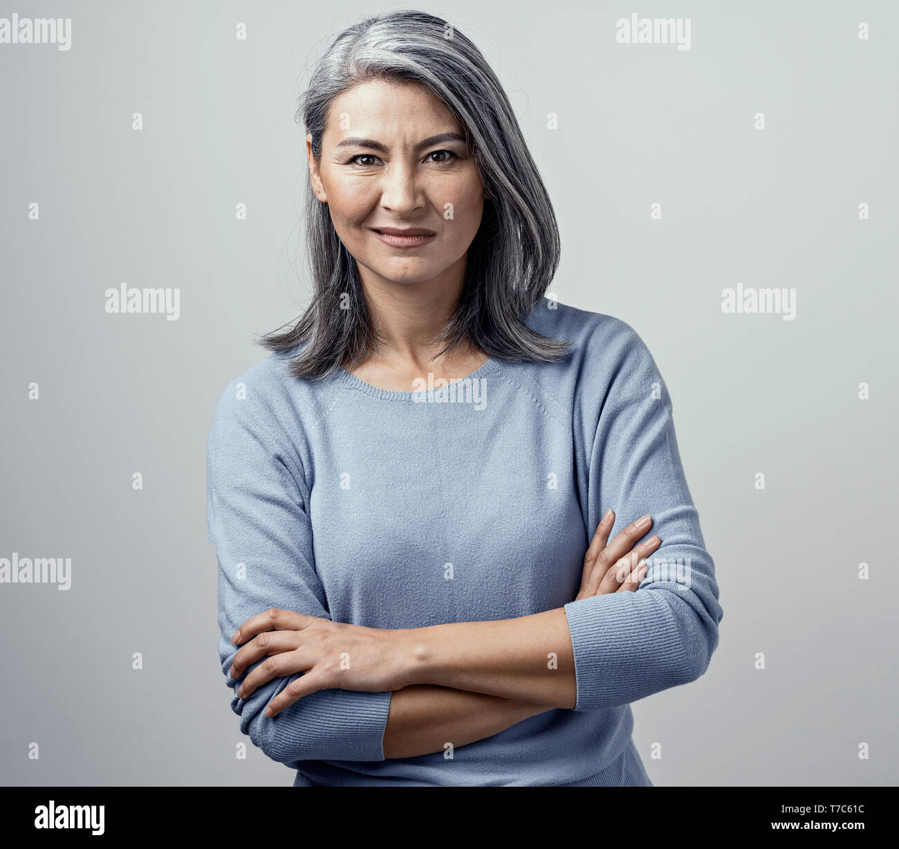 Attractive Elderly Female Model Posing Disgust and Dissatisfaction. Her Head Tilted and Hands Crossed. She has Middle-Length Grey Hair. Wears light-Bl Stock Photo