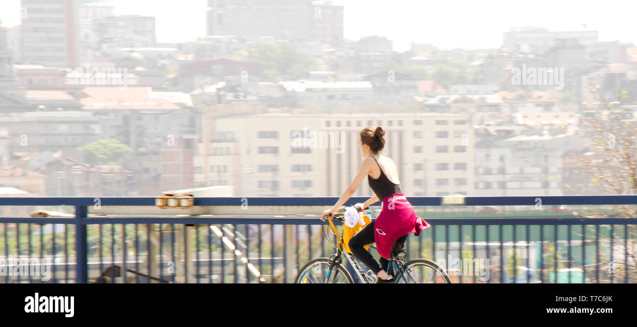 Belgrade, Serbia - April 25, 2019: One young woman riding bike on city street bridge with blurry bright cityscape background Stock Photo