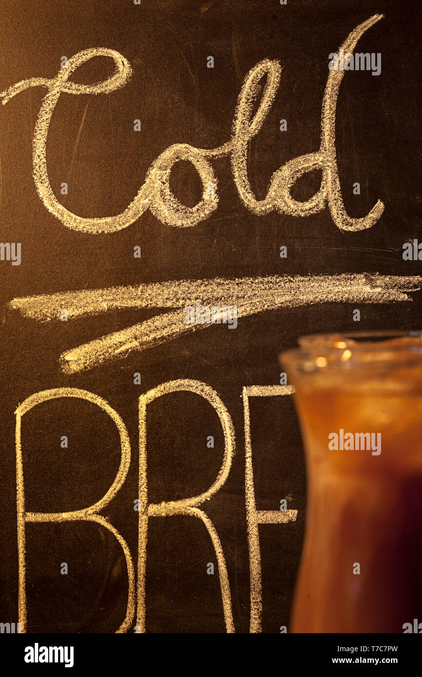 Cold brew coffee with writing on chalk board in background. Stock Photo