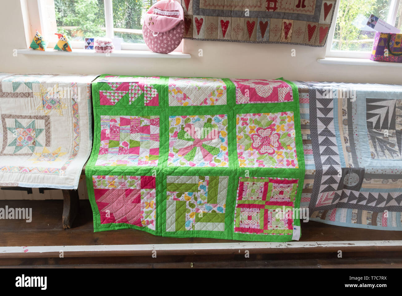 Homemade quilts on display in a village hall at the Oakhanger May Fayre in Hampshire, UK. Craft exhibition, sewing, needlework, handicrafts. Stock Photo