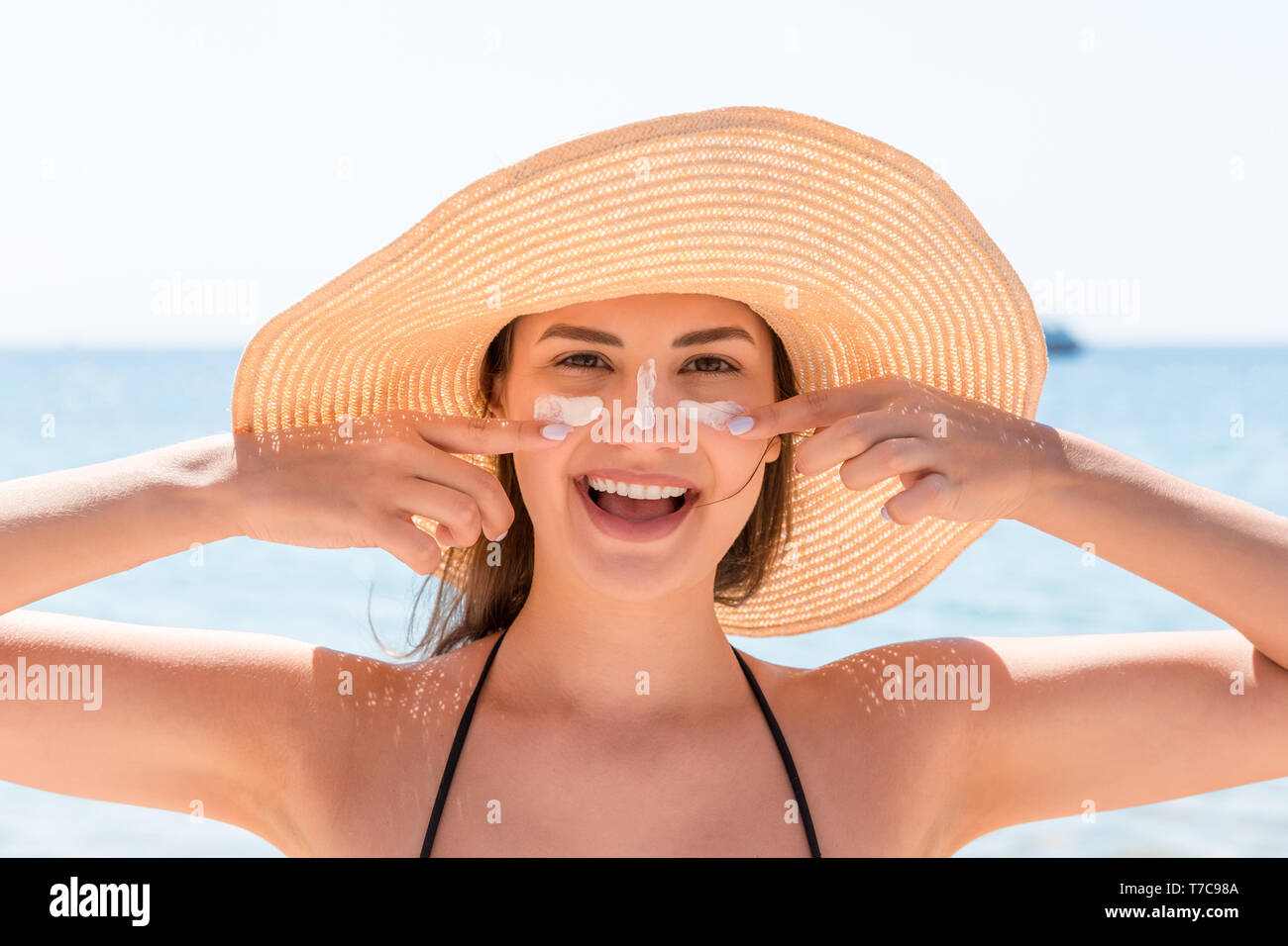 Beautiful young woman in hat is applying sunblock under her eyes and on