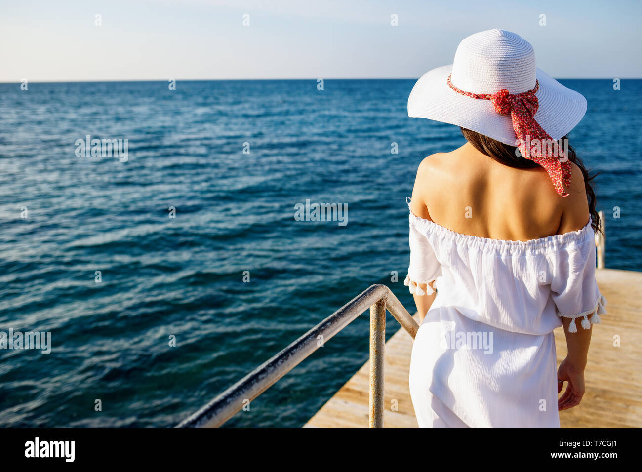 Back view on woman in white summer dress walking on wooden pier. Stock Photo
