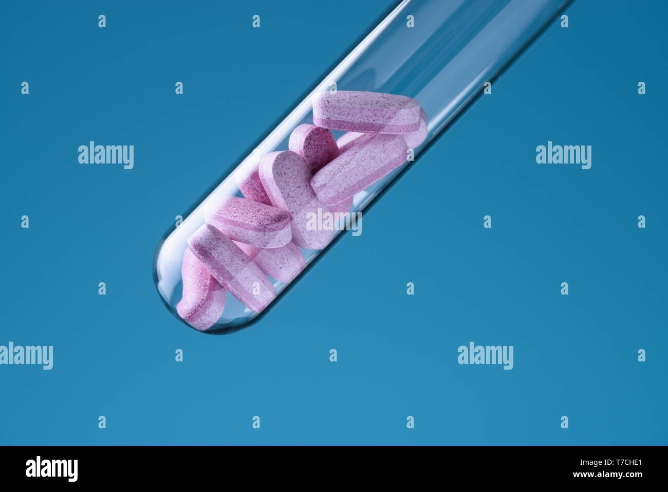 Laboratory glass test tube filled with pink pills on blue backround