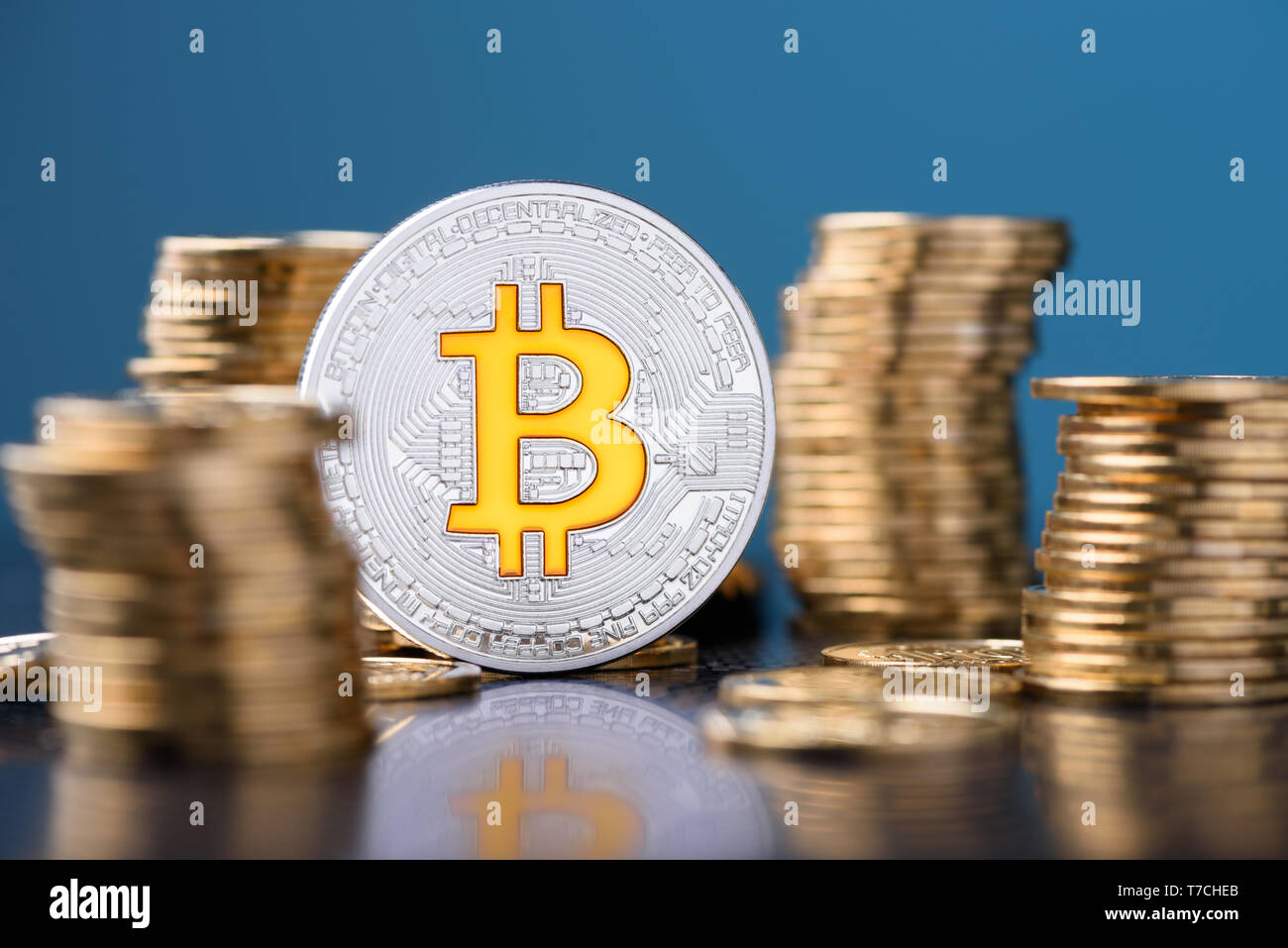 Bitcoin. Bitcoin coin between golden coins stacks with reflection. Stock Photo
