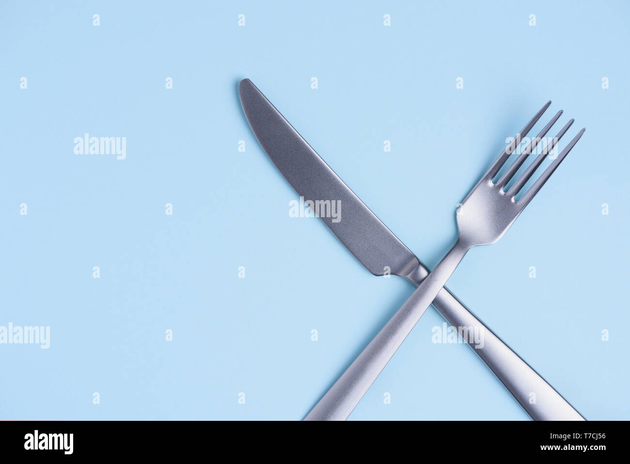 Crossed silver metal knife and fork sign on trendy blue pastel background with side copy space Stock Photo