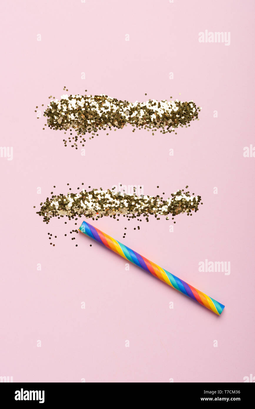 Golden glitter lines with a rainbow sniffing paper straw on pastel background. Party drugs concept. Stock Photo