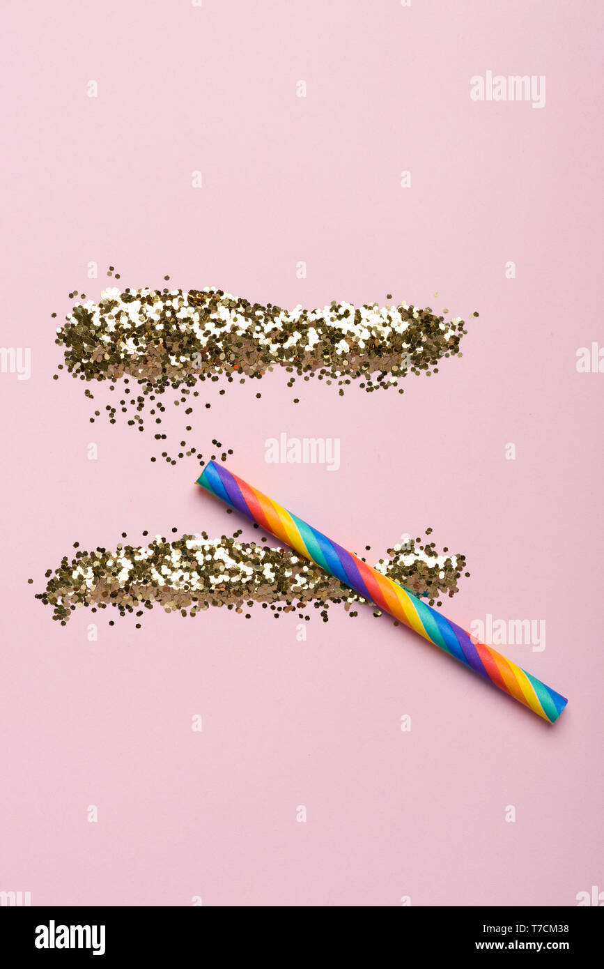 Shiny glitter lines with a rainbow sniffing paper straw on pastel background. Party drugs concept. Stock Photo