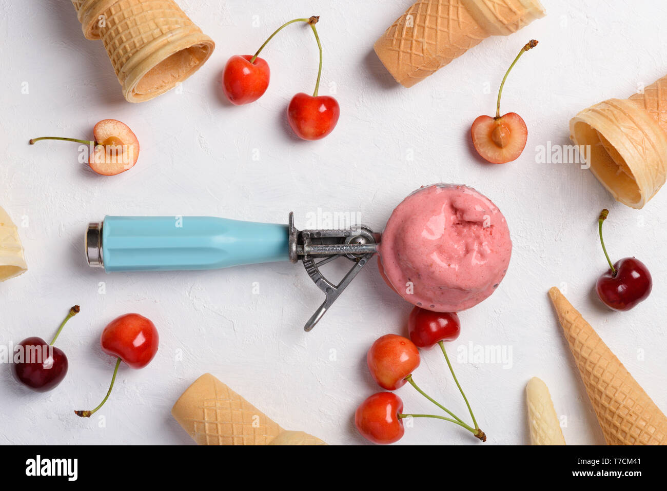 Homemade cherry ice cream scoop in spoon with waffle cones and ripe fresh cherries on white table flatlay top view Stock Photo