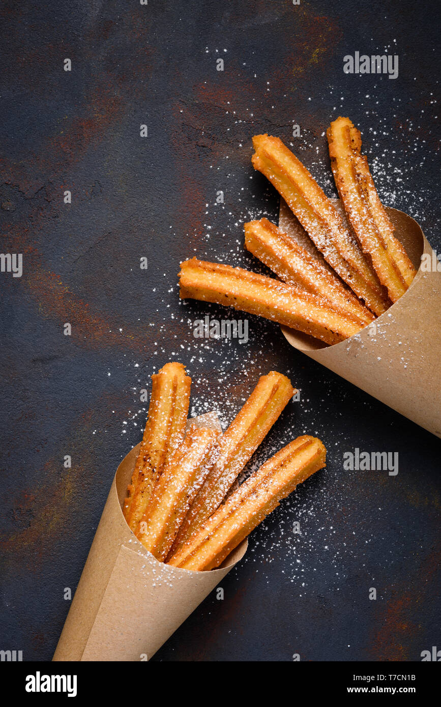 Churros sticks fresh hot with sugar powder and cinnamon in paper bag on dark background top view Stock Photo