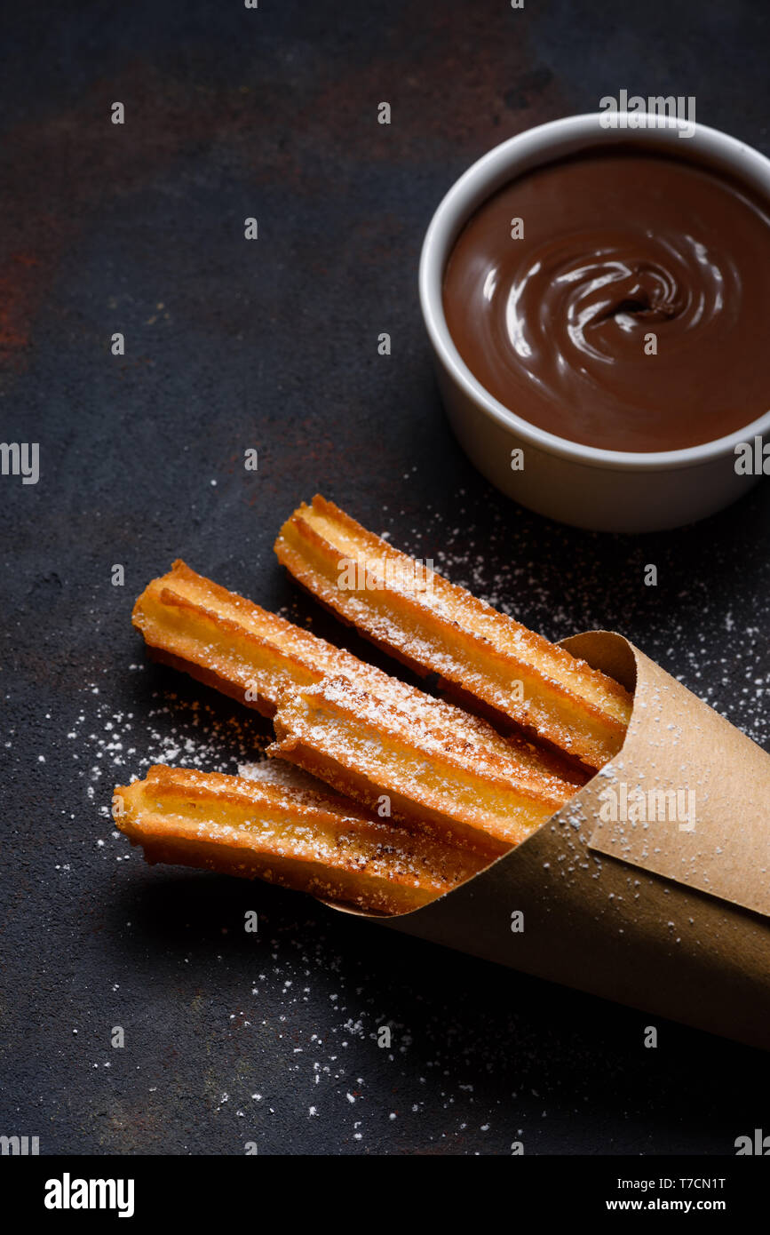 Churros in paper bag with sugar and chocolate sauce on dark black background Stock Photo
