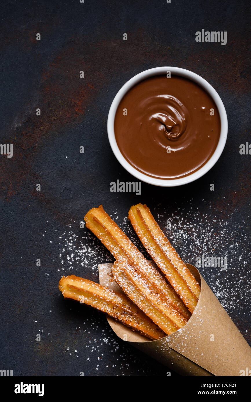 Churros in paper bag with sugar powder and chocolate sauce dip on dark black background Stock Photo