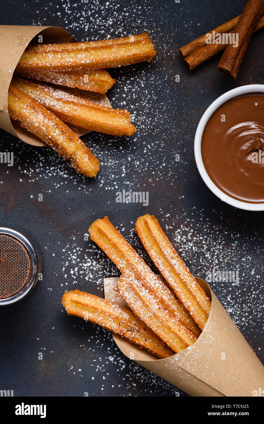 Churros with sugar powder chocolate sauce dip and cinnamon sticks on dark background flat lay top view Stock Photo