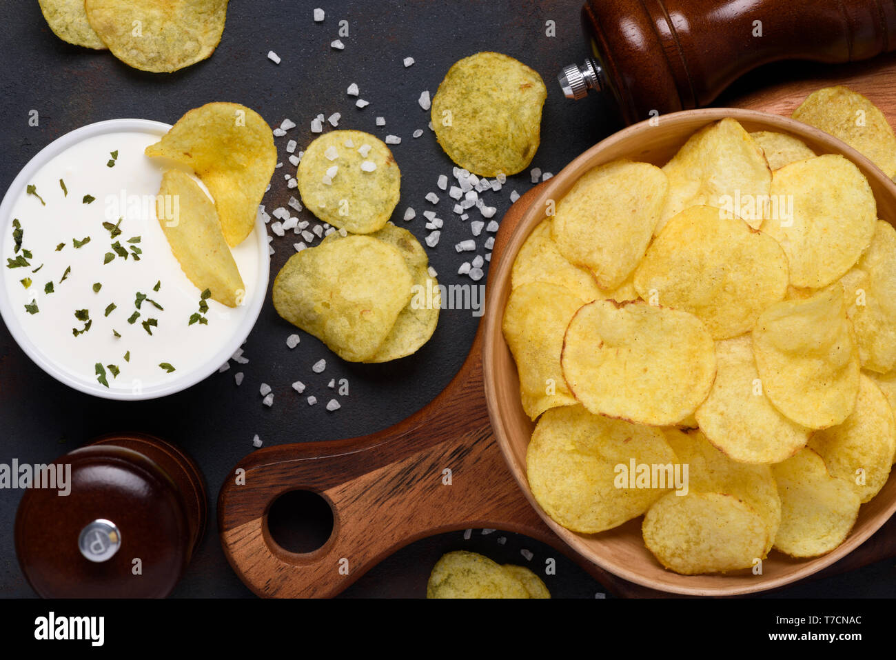 Crispy potato chips in bowl with dip and salt on dark table top view Stock Photo