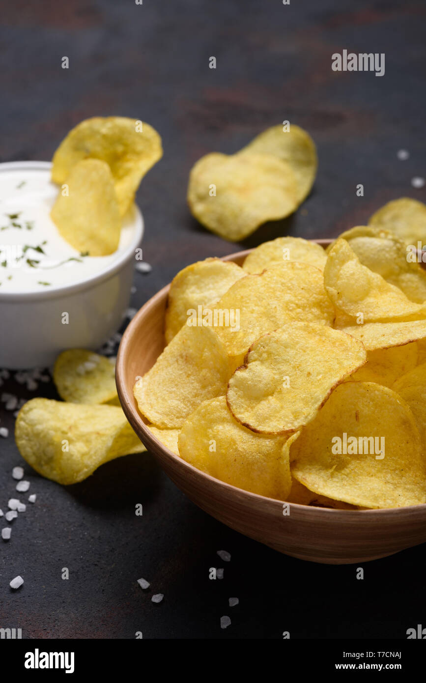 Crispy potato chips in bowl with sauce dip and salt on dark table Stock Photo