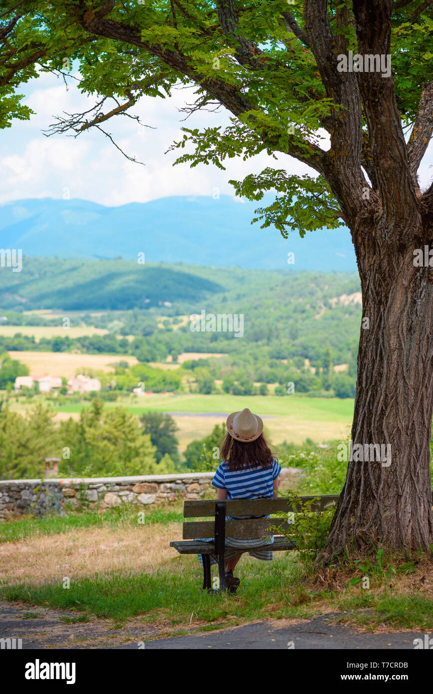 Woman in dress sitting on a bench under the tree overlooking valley and ...