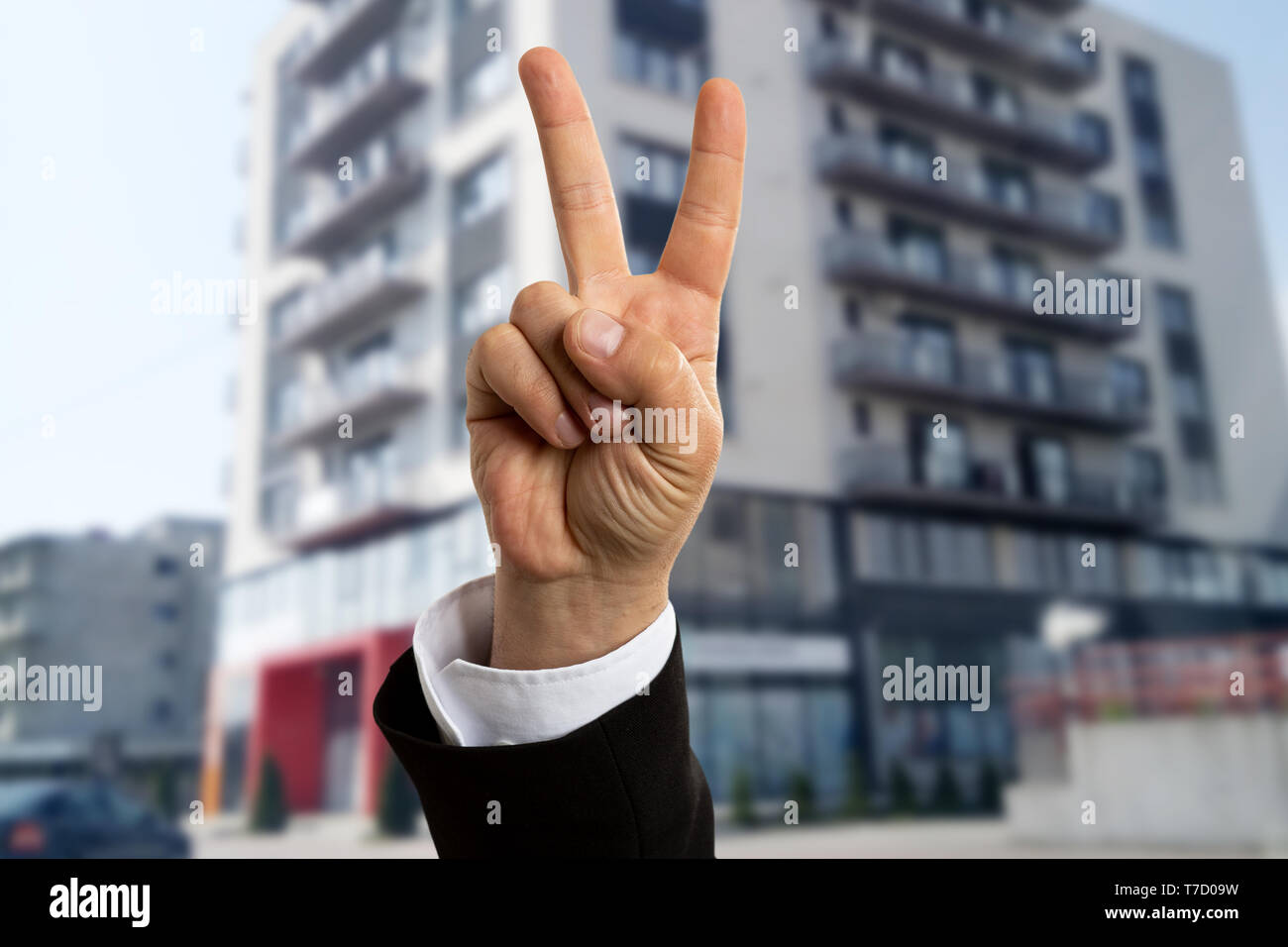 Male real estate agent showing victory or peace sign in front of