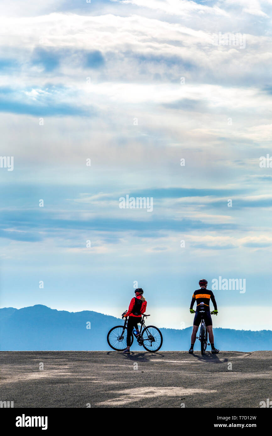 A couple on bicycles looking over a scenic mountain view, cycling in Mount Fløyen in Bergen, Norway Stock Photo