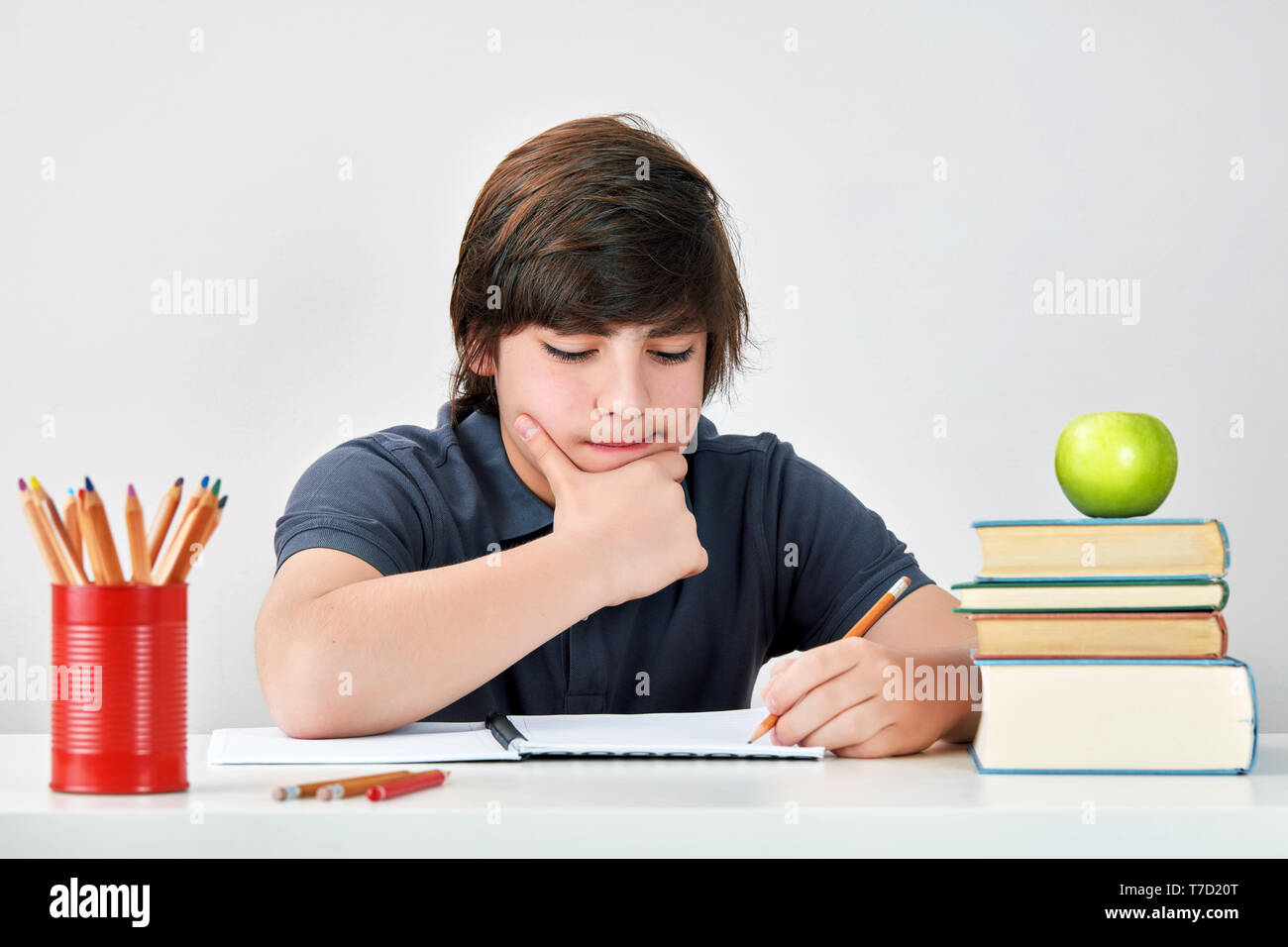 Caucasian school boy sitting at the table and thinking with a serious and concentrated expression while doing his homework. Stock Photo