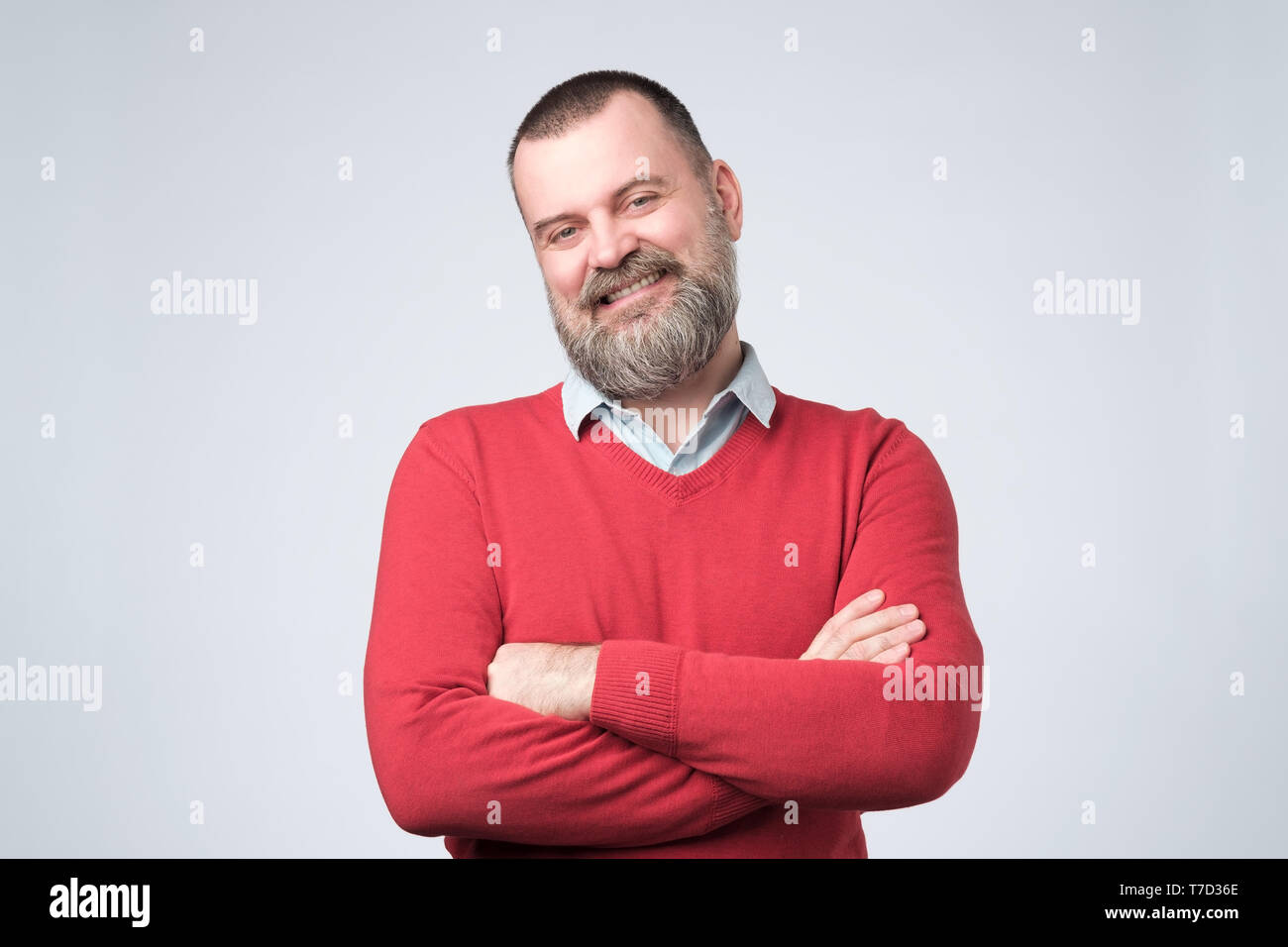 Mature man with beard holding hands crossed and looking at camera while smiling Stock Photo