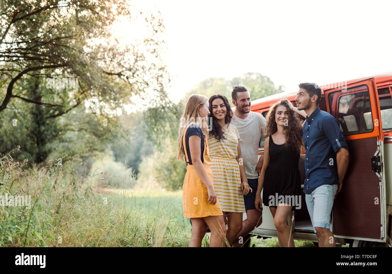 A group of young friends standing by a retro minivan on a roadtrip ...