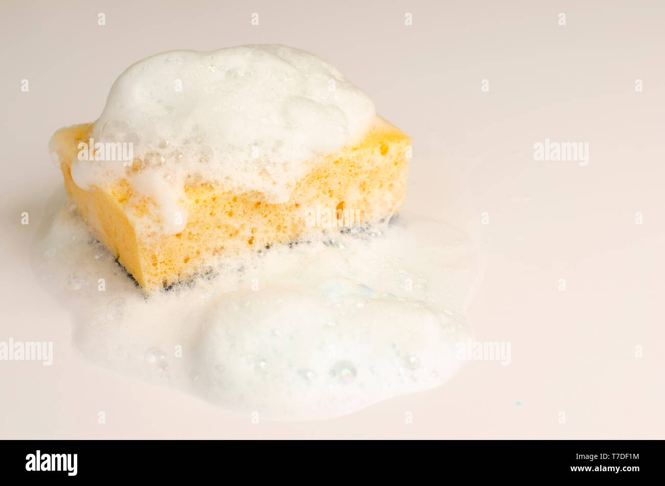 Yellow soapy sponge with foam on white background. Copy space. Stock Photo