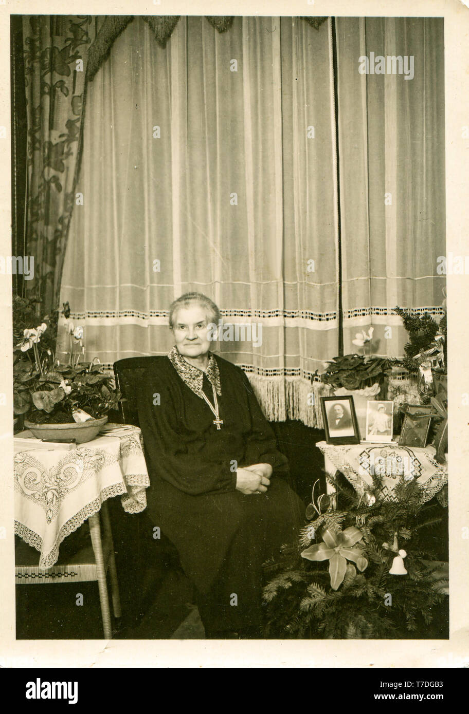 Elderly woman celebrates Christmas. On the table is a portrait of a deceased husband and portreya family. Germany 1940s. Stock Photo